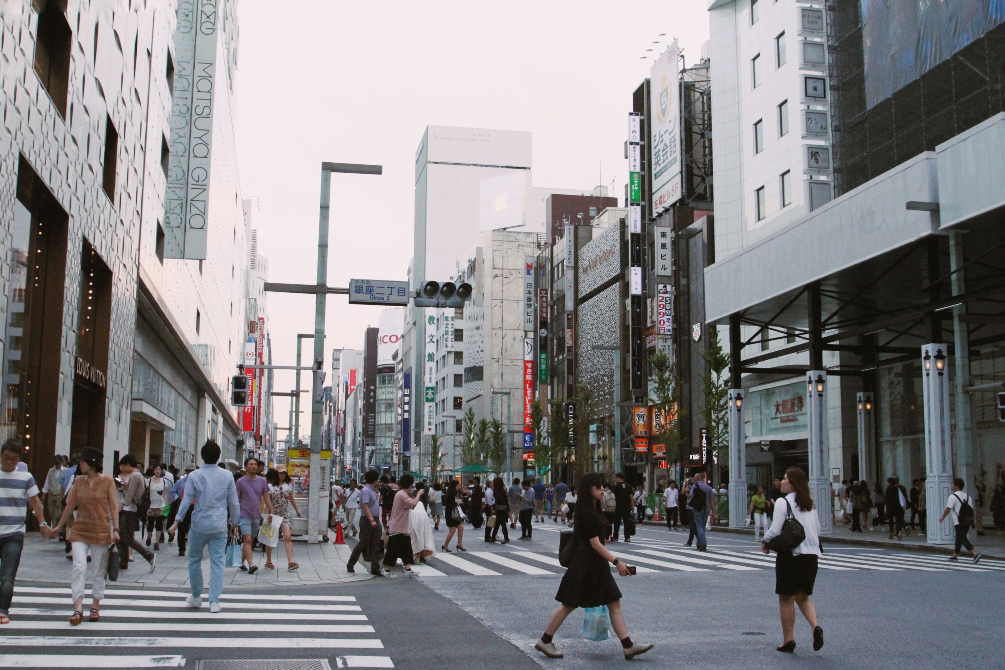 Pedestrians walk through Tokyo's Ginza district lined with modern buildings.