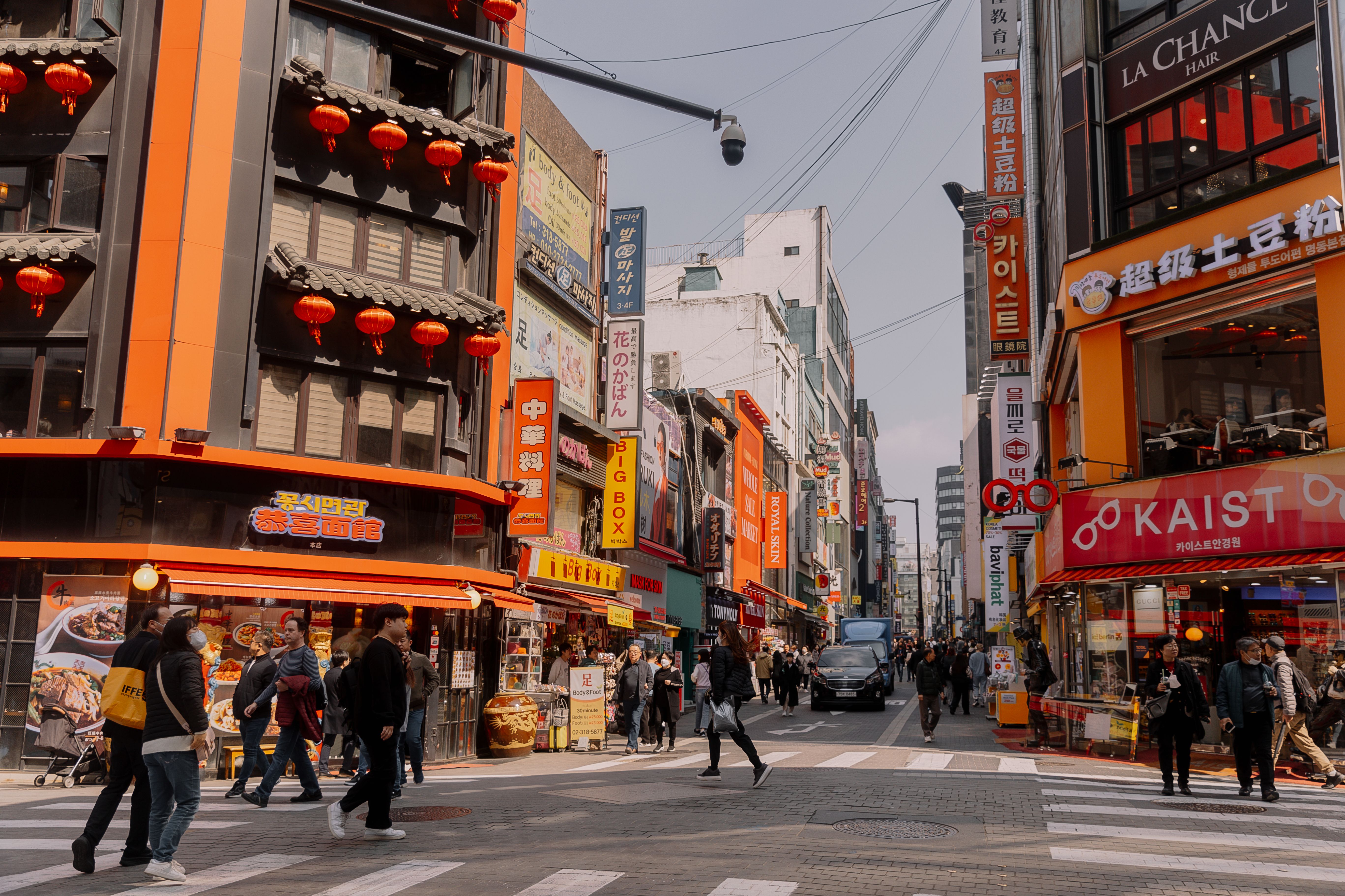 首尔明洞街景，商店和餐厅林立，人流熙攘。